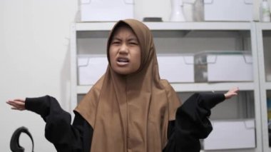 Genç Asyalı Müslüman kadın, kafası karışmış bir ifadeyle omuz silkiyor.