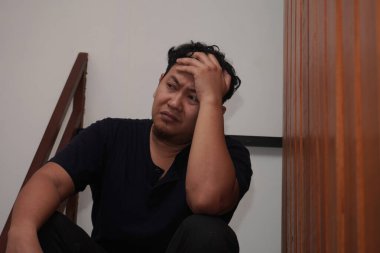 Üzgün Asyalı adam evinde merdivenlerde oturuyor, umutsuzluk hayal kırıklığı stres kaybı, hayat sorunları konsepti.