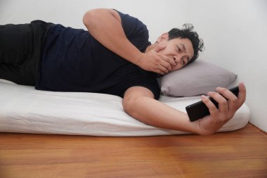Yetişkin bir Asyalı sabah yataktan kalktıktan sonra telefonunu kontrol ediyor.