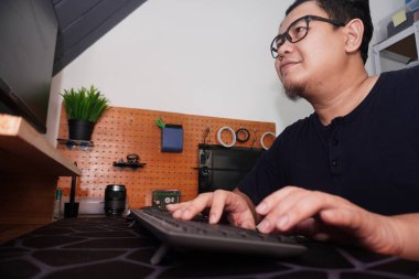 Yetişkin Asyalı adam evde bilgisayarında daktilo yazıyor, uzaktan çalışan serbest çalışan, online iş kavramı, mutlu gülümseme ifadesi.