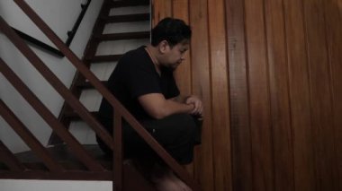 Üzgün Asyalı adam evinde merdivenlerde oturuyor, umutsuzluk hayal kırıklığı stres kaybı, hayat sorunları konsepti.