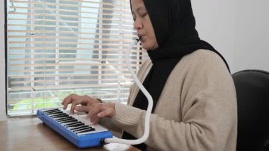 Asya 'lı Müslüman kadın tesettüre girmiş piyano çalıyor, melodi üfleme organı enstrümanı çalıyor