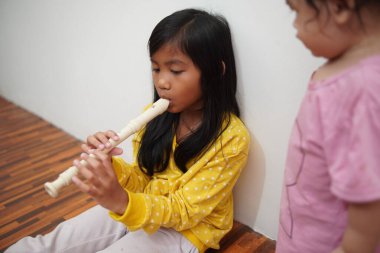 Küçük tatlı Asyalı kız, küçük kız kardeşi için flüt çalıyor, müzik aleti.