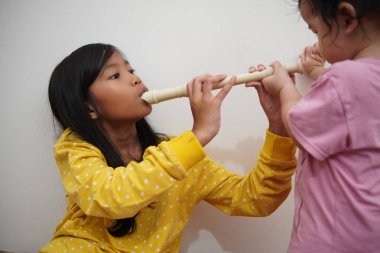 Küçük tatlı Asyalı kız, küçük kız kardeşi için flüt çalıyor, müzik aleti.