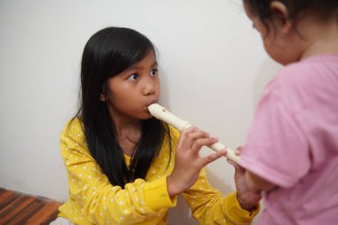 Küçük tatlı Asyalı kız, küçük kız kardeşi için flüt çalıyor, müzik aleti.