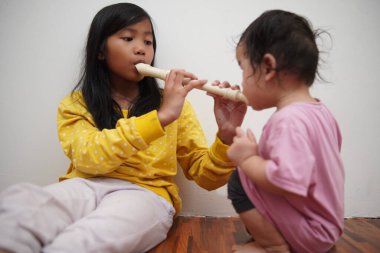 Küçük tatlı Asyalı kız, küçük kız kardeşi için flüt çalıyor, müzik aleti.