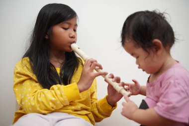 Küçük tatlı Asyalı kız, küçük kız kardeşi için flüt çalıyor, müzik aleti.