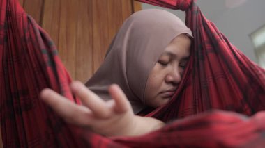Asyalı Müslüman anne, bebeğini salıncakta sallarken yorgun ve uykulu görünüyor. Doğum sonrası depresyon