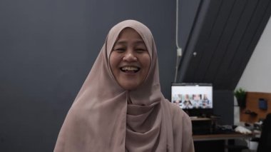 Mutlu, kendinden emin, Asyalı Müslüman kadın kameraya bakarken gülüyor, portreyi kapatıyor.