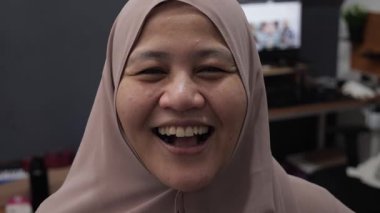 Mutlu, kendinden emin, Asyalı Müslüman kadın kameraya bakarken gülüyor, portreyi kapatıyor.