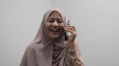 Mutlu gülümseyen Asyalı Müslüman kadın telefonda konuşurken gülüyor, iyi haberler alıyor.