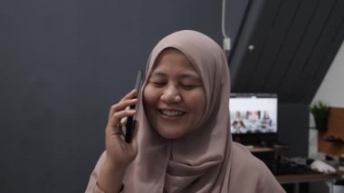 Mutlu gülümseyen Asyalı Müslüman kadın telefonda konuşurken gülüyor, iyi haberler alıyor.