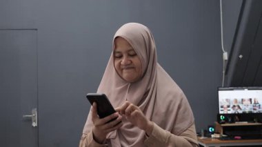 Asyalı Müslüman kadın, akıllı telefonuna baktığında hayal kırıklığına uğramış görünüyor.