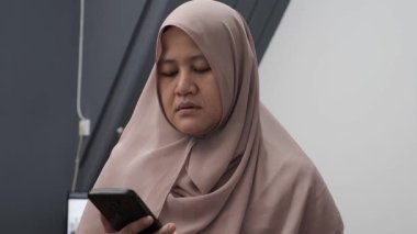 Asyalı Müslüman kadın, akıllı telefonuna baktığında hayal kırıklığına uğramış görünüyor.