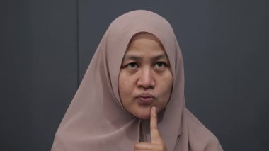 Asyalı Müslüman kadın gülümseyen bir şey düşünüyor, mutlu pozitif, iyi fikir ifadesini işaret ediyor.