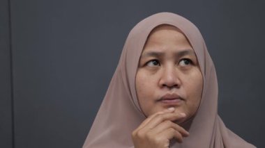 Asyalı Müslüman kadın gülümseyen bir şey düşünüyor, mutlu pozitif, iyi fikir ifadesini işaret ediyor.