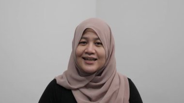 Asyalı Müslüman kadın kameraya konuşuyor, bir şeyler anlatıyor ya da konuşma yapıyor, mutlu bir gülümseme.