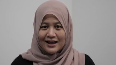 Asyalı Müslüman kadın kameraya konuşuyor, bir şeyler anlatıyor ya da konuşma yapıyor, mutlu bir gülümseme.