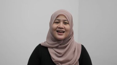 Asyalı Müslüman kadın kameraya konuşuyor, bir şeyler anlatıyor ya da konuşma yapıyor, mutlu bir gülümseme.