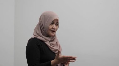 Asyalı Müslüman kadın konuşuyor, bir şeyler anlatıyor ya da konuşma yapıyor, yan görüş, mutlu gülümseme ifadesi.
