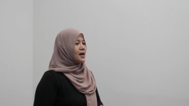 Asyalı Müslüman kadın konuşuyor, bir şeyler anlatıyor ya da konuşma yapıyor, yan görüş, mutlu gülümseme ifadesi.