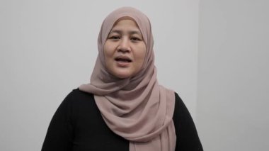 Asyalı Müslüman kadın kameraya konuşuyor, bir şeyler anlatıyor ya da konuşma yapıyor, mutlu bir gülümseme.