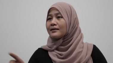 Asyalı Müslüman kadın konuşuyor, bir şeyler anlatıyor ya da konuşma yapıyor, yan görüş, mutlu gülümseme ifadesi.