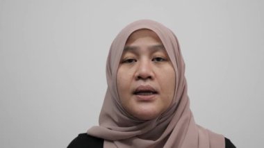 Asyalı Müslüman kadın kameraya konuşuyor, bir şeyler anlatıyor ya da konuşma yapıyor, mutlu bir gülümseme.