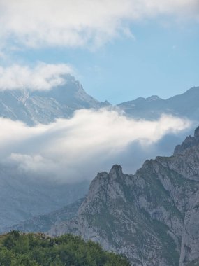 Picos de Europa 'daki engebeli kireçtaşı tepeleri - Sivri kireçtaşı tepeleri, yeşil yamaçları ve İspanya' nın Asturias şehrinde alçaktan sarkan bulutlarla görkemli ve dramatik dağ manzarası.