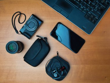 Overhead Tech Gear Creative Workspace - Ahşap bir masanın üstünde kamera, lens, akıllı telefon, kulaklık ve dizüstü bilgisayar. Fotoğraf, yaratıcı iş, seyahat ve dijital göçebe yaşam tarzı kavramı.