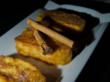 Tarçın çubuklu İspanyol tostu. Şeker ve tarçınlı geleneksel İspanyol torrijaları. Beyaz tabakta servis ediliyor..