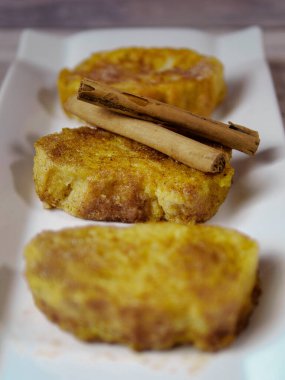 Tarçın çubuklu İspanyol tostu. Şeker ve tarçınlı geleneksel İspanyol torrijaları. Beyaz tabakta servis ediliyor..