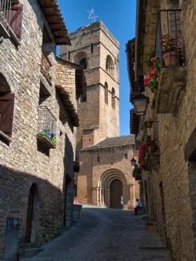 Ortaçağ Kilise Kulesi 'ne giden Dar Sokak - Cobblestone Caddesi ve Romanesk büyük bir kilise kulesine çıkan uzun taş köy evleri ve berrak mavi gökyüzünün altındaki kemerli giriş..