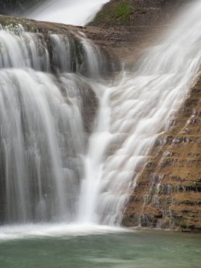 Şelalenin Kayalıklardan Aşağı Şelale 'ye yakın çekim - Uzun pozlama kullanarak ipeksi, pürüzsüz bir su efekti yaratarak dokuma, kırmızımsı kahverengi kaya oluşumlarını havuza doğru akıtmak.