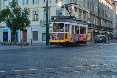 Cobbled Caddesi 'ndeki ikonik Sarı Lizbon Tramvayı klasik Carrera 28 tramvayı geleneksel binalar ve kaldırım taşlarıyla tarihi bir caddede ilerliyor..