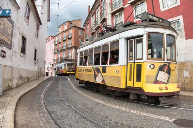 Cobbled Caddesi 'ndeki ikonik Sarı Lizbon Tramvayı klasik Carrera 28 tramvayı geleneksel binalar ve kaldırım taşlarıyla tarihi bir caddede ilerliyor..