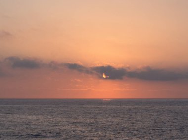 Yumuşak Şeftali Günbatımı Okyanus Ufkunu Üzerindeki Ufkunda - Sakin deniz manzarası batan güneşin okyanus ufkunun üzerinden karanlık bulutlara baktığını gösteriyor, şeftali ve turuncu bir parıltı yayıyor.