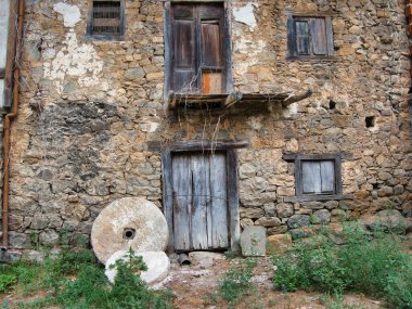 Öğütülmüş Taştan Değirmen Evi eski ahşap kapıları ve dışarıda iki antika değirmen taşı olan terk edilmiş taştan bir binanın cephesi..