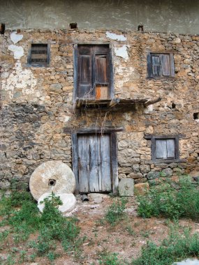 Millstone ve Doors 'lu Antik Taş Ev - Kırsal kesimde terk edilmiş taştan duvarlı ön cephe, yıpranmış ahşap kapılar ve pencereler, ve ön planda tarihi değirmen taşları.