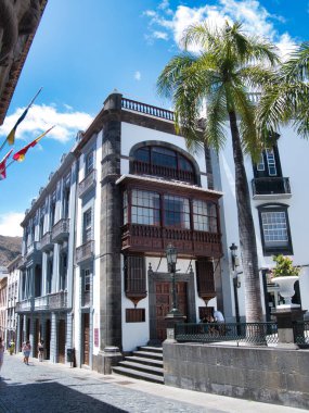 Tarihsel Kanarya Adası Balkon Mimarisi - Geleneksel İspanyol sömürge mimarisi çarpıcı ahşap bir balkonu ve mavi gökyüzünün altındaki kaldırım taşı bir sokakta palmiye ağacı.