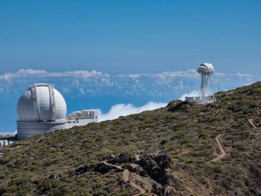 Tepedeki Beyaz Küresel Teleskop Kubbesi - Küresel bir kubbesi olan büyük beyaz astronomik gözlemevi bir dağ sırtına kurulmuş, bulutlara ve derin mavi okyanusa bakan.