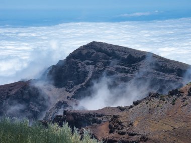 Beyaz Bulut Denizi 'ne Bakan Volkanik Tepe - Derin mavi bir gökyüzünün altında geniş, yoğun beyaz bulutlar denizine bakan kırmızı ve gri volkanik kayalardan oluşan geniş bir dağ manzarası.