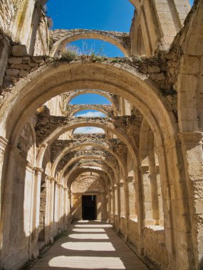 Antik taş kemer ve manastırların geniş perspektifi - Tarihi bir manastır veya manastırın mimari kalıntıları açık kemerlerden ve mavi gökyüzünden akan güneş ışığıyla.