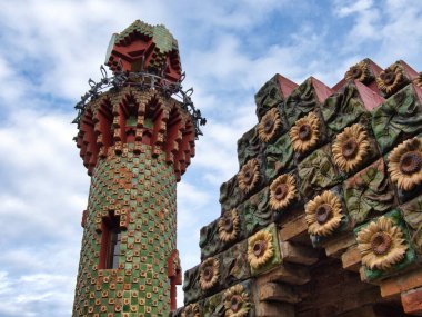 Gaud-Style Modernist Kulesi ve Ayçiçeği Detaylı Detay Seramik döşemeli bir kule ve tekrarlanan ayçiçeği kabartmaları ve kırmızı tuğlalardan oluşan Cornice manzarası.