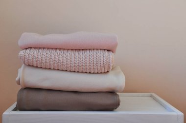 Açık beyaz ahşap masada bir yığın kalın kazak ve pantolon. Metin için boşluk