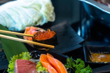 Yemek çubuklarıyla suşi yemek. Suşi restoranda Japon yemeği yapar. Somon, sebze, uçan balık yumurtası ve havyar kapaklı. Japon restoran menüsü