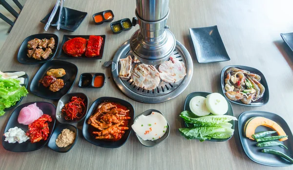 Korea BBQ style restaurant. Asian traditional pickle vegetable ingredients on table with people grilling background.