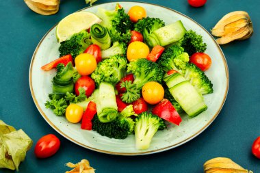 Fresh salad with broccoli, tomato, physalis and cucumber on the plate. Vegetarian food