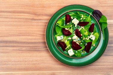 Healthy salad with beets, blue cheese, herbs and pine nuts on wooden table. Copy space