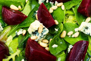 Delicious salad with boiled beets, blue cheese, greens and pine nuts. Closeup